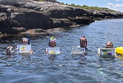 4 students in the tide pool holding up artwork, wearing snorkling gear